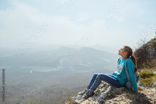 A girl in the mountains sits on a rock and looks at the surrounding landscape. Active sports and recreation.