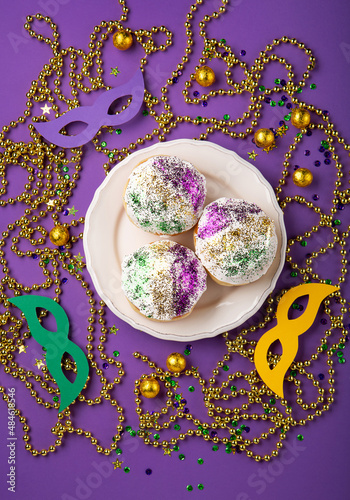 Fotografie, Obraz Mardi Gras King Cake sufganiyot donuts, masquerade festival carnival masks, gold beads and golden, green, purple confetti on purple background