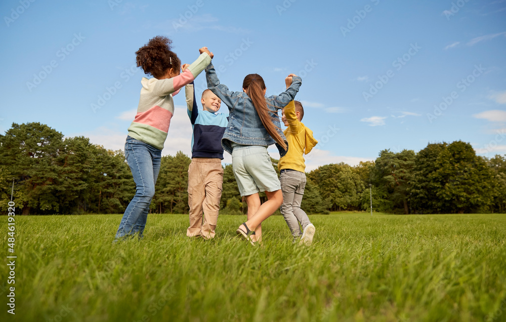 childhood, leisure and people concept - group of happy kids playing round dance at park childhood, leisure and people concept - group of happy kids playing round dance at park