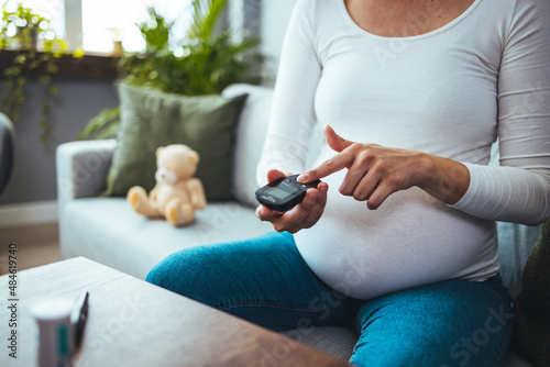Pregnancy, health and glycemia concept - pregnant beautiful woman checking blood sugar level with glucometer and lancing device at home