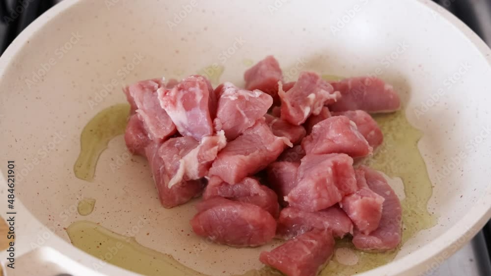 Frying pieces of raw veal meat in white frying pan with heated olive oil close up, concept of cooking at home in the kitchen Frying pieces of raw veal meat in white frying pan with heated olive oil close up, concept of cooking at home in the kitchen