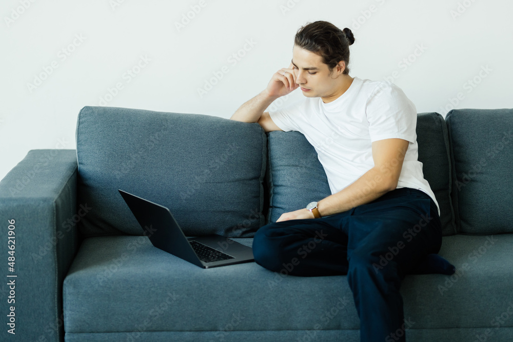 Attractive young man relaxing on a couch at home, working on laptop Attractive young man relaxing on a couch at home, working on laptop