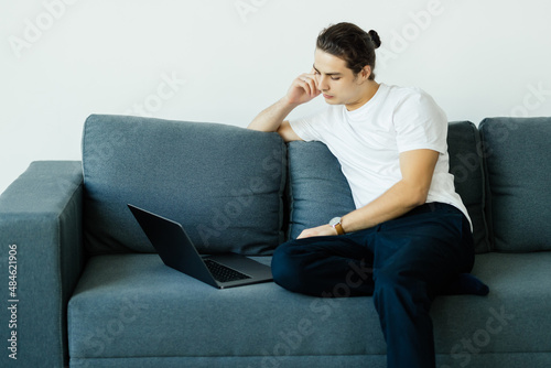 Attractive young man relaxing on a couch at home, working on laptop