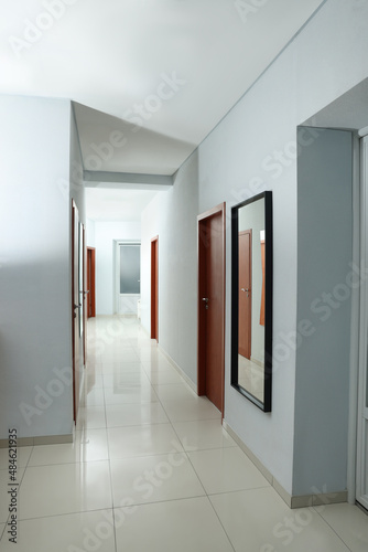 Modern empty office corridor with white walls and mirror