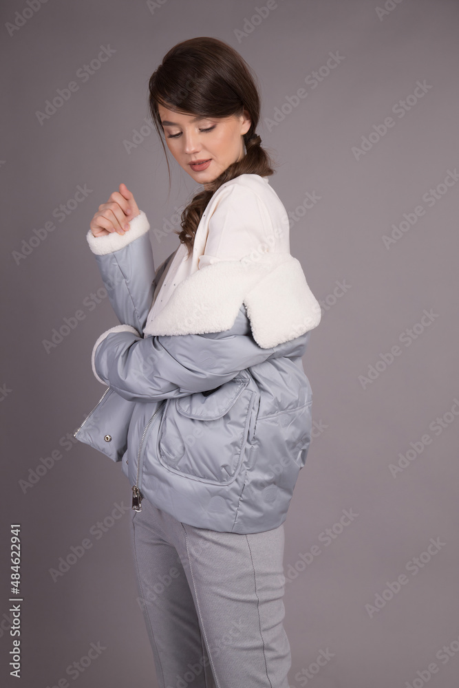 A young girl model posing at the camera demonstrates clothes in different positions.Shooting in a clothes studio on a gray background showing a model. A young girl model posing at the camera demonstrates clothes in different positions.Shooting in a clothes studio on a gray background showing a model.