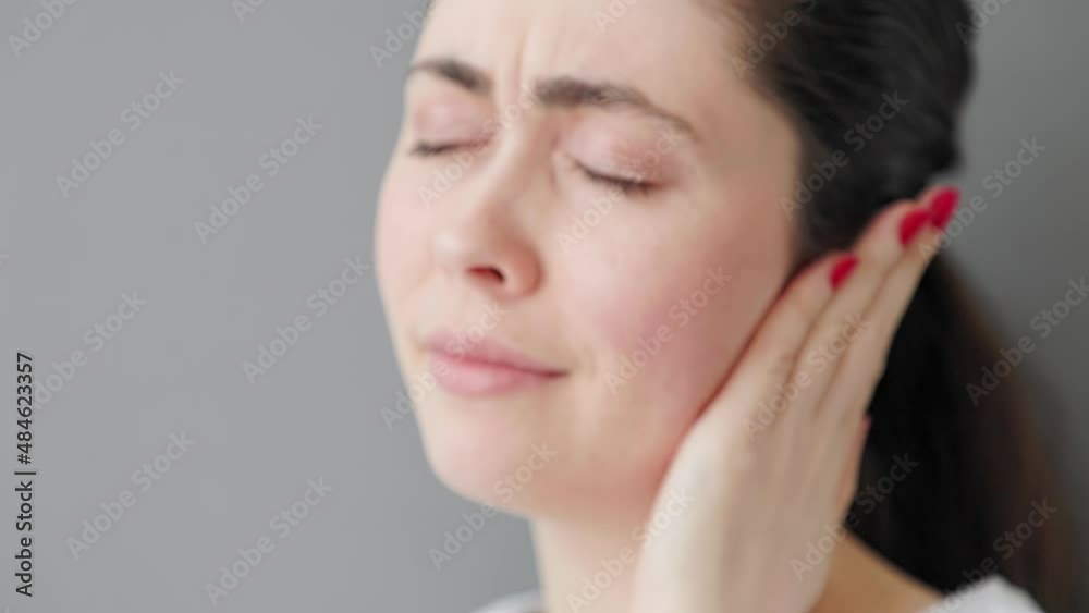 Portrait of a young Caucasian beautiful woman suffering from ear pain. Gray background. The concept of deafness and ear diseases. Portrait of a young Caucasian beautiful woman suffering from ear pain. Gray background. The concept of deafness and ear diseases.