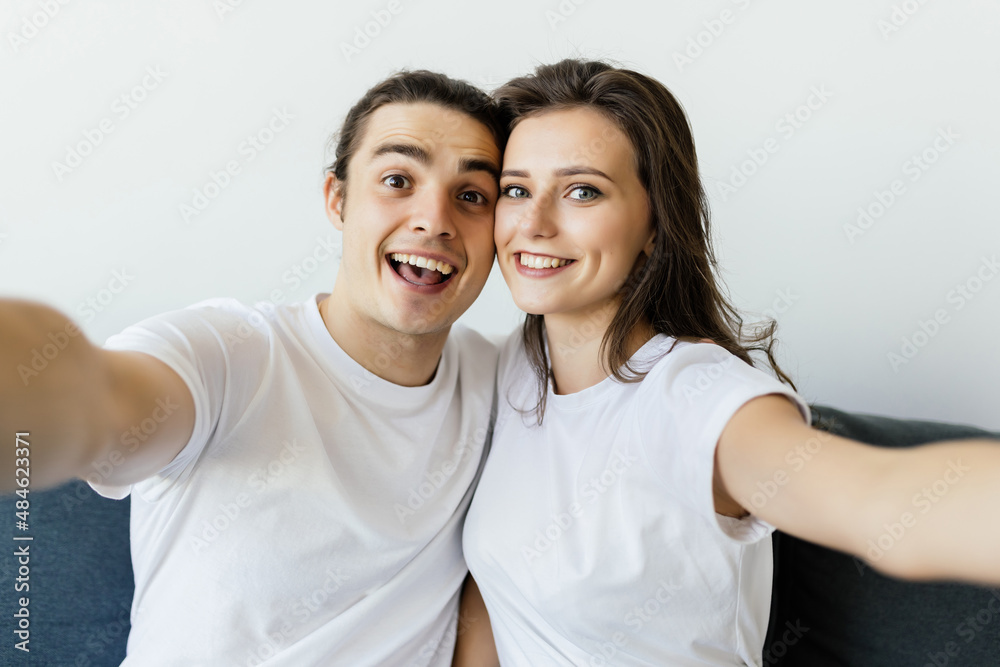 Beautiful young loving couple bonding to each other and making selfie while sitting on the couch together Beautiful young loving couple bonding to each other and making selfie while sitting on the couch together
