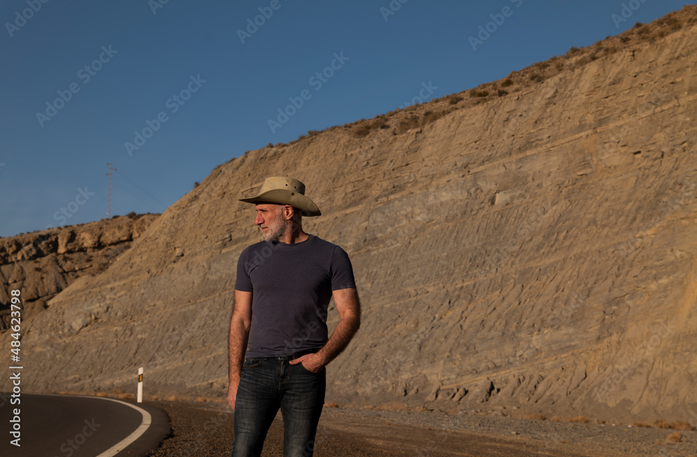 Adult man in cowboy on roadside on desert against mountain. Almeria, Spain Adult man in cowboy on roadside on desert against mountain. Almeria, Spain