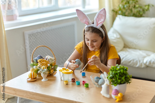 Cute little child wearing bunny ears. Kid is painting eggs.