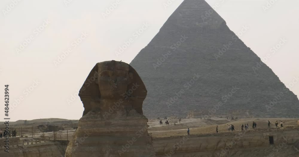 Smooth transition from the Sphinx to the Great Pyramid of Giza in Cairo, Egypt. Clear day, tourists in the background. Wide shot, slow motion Smooth transition from the Sphinx to the Great Pyramid of Giza in Cairo, Egypt. Clear day, tourists in the background. Wide shot, slow motion