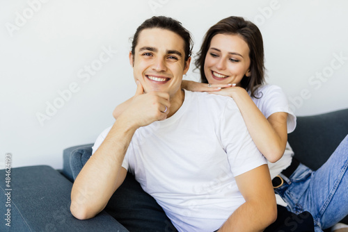 Happy young couple of man and woman embracing look at each other sitting on couch in living room.