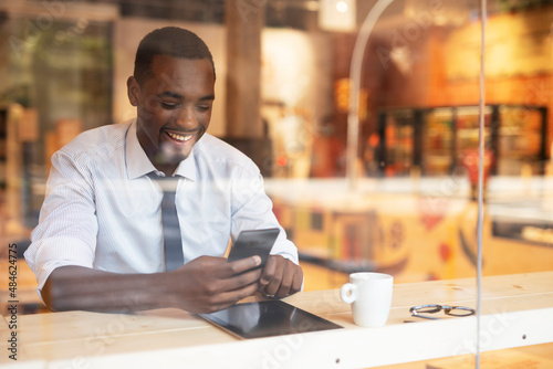 Businessman drinking coffee in cafe. Handsome African man using the phone while enjoying in fresh coffee.