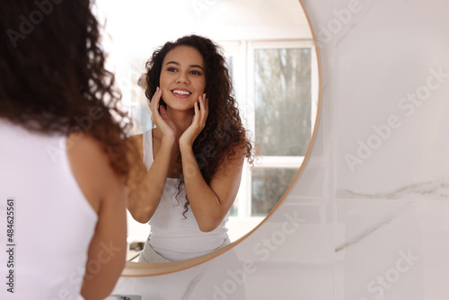 Beautiful African American woman near mirror in bathroom, space for text