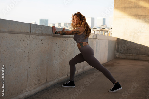 Beautiful young woman with curly hair training outside. Fit sexy woman doing exercise.