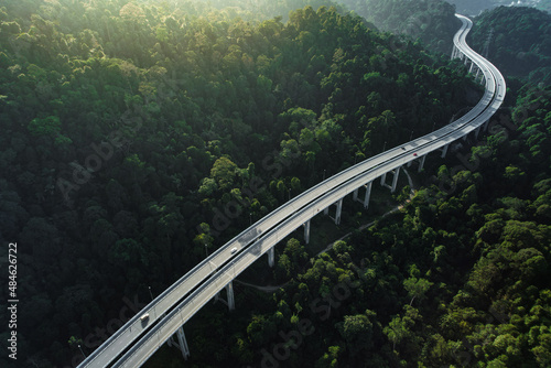 aerial shot of  car using elevated highway road across a green forest in the morning with mist