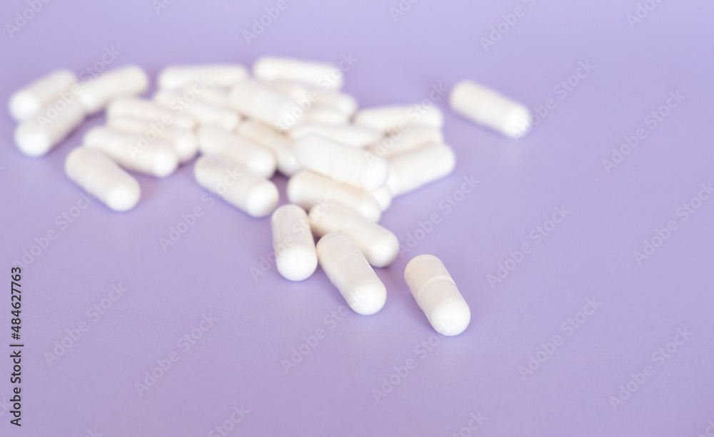 Close up white pills and capsules on purple background with copy space. Focus on foreground, soft bokeh. Pharmacy drugstore concept. Close up white pills and capsules on purple background with copy space. Focus on foreground, soft bokeh. Pharmacy drugstore concept.