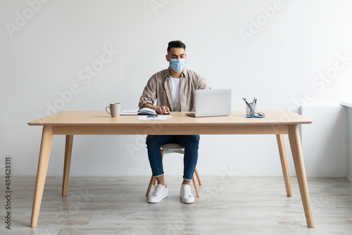 Man in protective facemask working on pc at home office