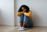 Unhappy young black woman sitting on floor, feeling depressed at home, copy space
