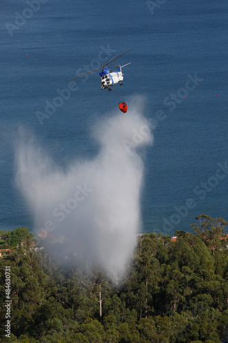 A firefighting helicopter drops water on a forest fire