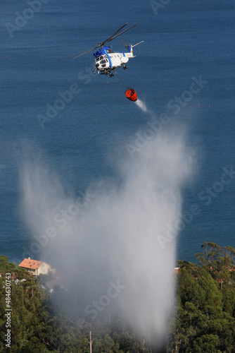 A firefighting helicopter drops water on a forest fire