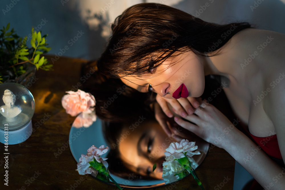 Naklejka premium Girl fashion portrait looks in mirror. Attractive young brunette with red lips. Female self love, esteem and confidence. Believe in yourself. Plastic surgery, beauty, makeup