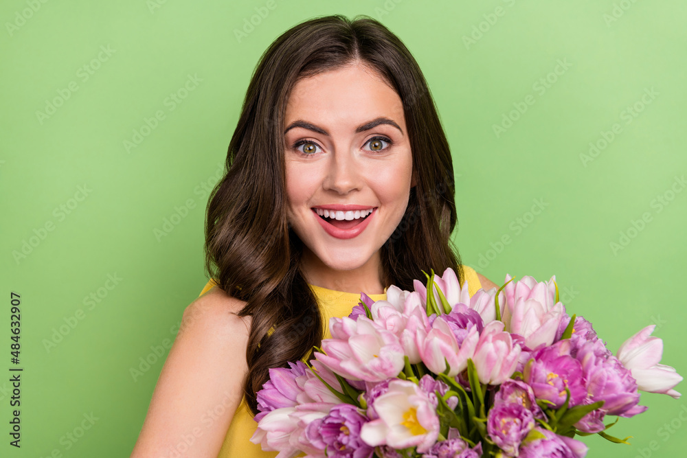 Portrait of attractive cheerful wavy-haired girl holding flowers having fun isolated over bright green color background