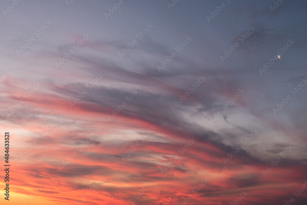 moon in the sky during sunset and clouds in orange and gray colors