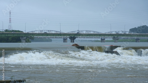 豪雨で増水した河川。橋を渡る車。
