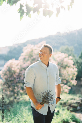 Smiling man with a bouquet of lavender in his hand stands near a blossoming tree