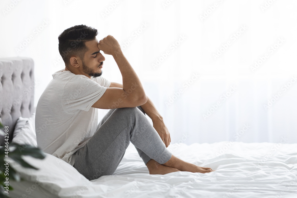 Portrait Of Depressed Young Middle Eastern Man Sitting On Bed In Bedroom Portrait Of Depressed Young Middle Eastern Man Sitting On Bed In Bedroom