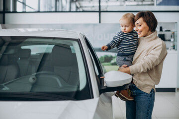 Woman with baby son choosing a car in a car salon