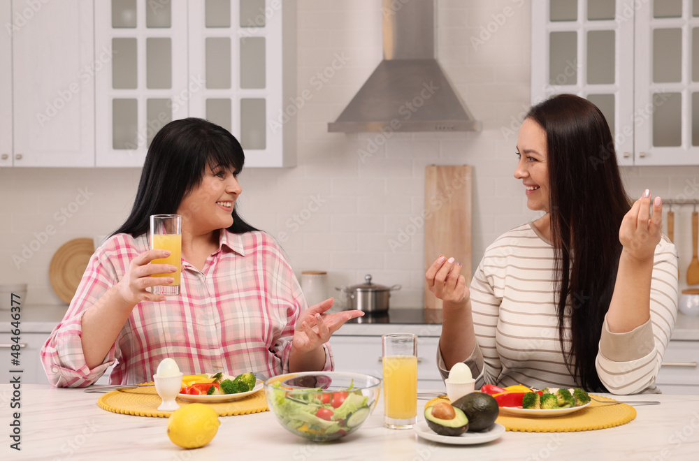 Happy overweight women having healthy meal together at table in kitchen Happy overweight women having healthy meal together at table in kitchen