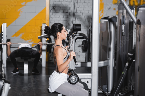 Middle east woman with dumbbell training on lat pulldown machine in gym.
