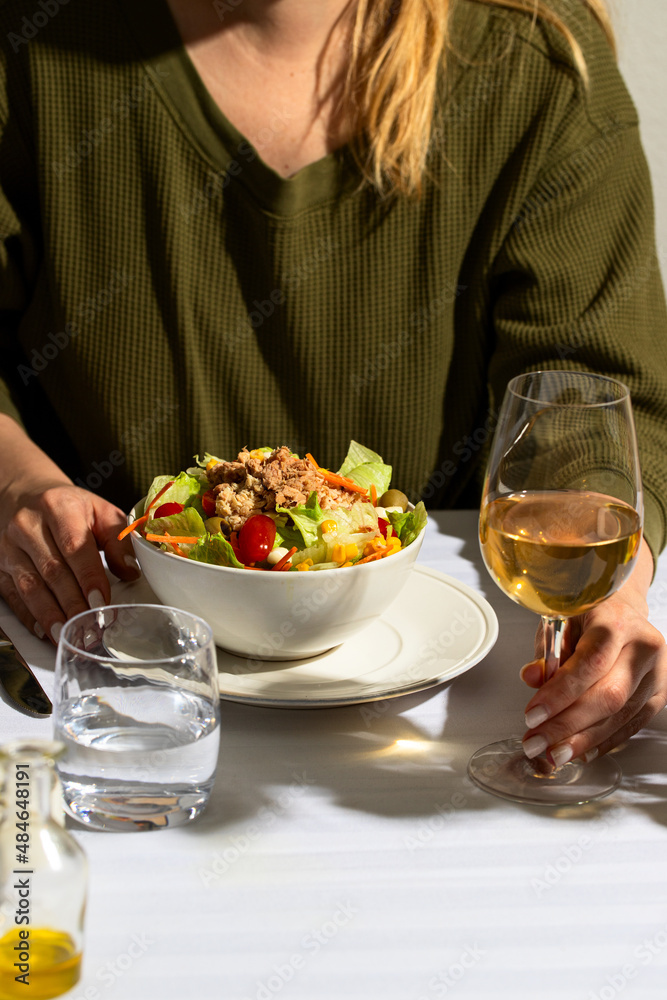 Woman sitting in the ristorante and eating classic Tuna salad, served with with glass water and white wine Woman sitting in the ristorante and eating classic Tuna salad, served with with glass water and white wine