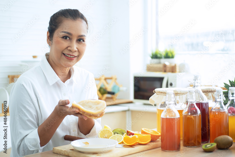 Middle age woman show Scoby or fungus on plate near Kombucha drink bottle in her kitchen, Scoby tea mushroom to start the fermentation process to make Kombucha Middle age woman show Scoby or fungus on plate near Kombucha drink bottle in her kitchen, Scoby tea mushroom to start the fermentation process to make Kombucha