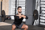Arabian sportsman training with barbell in blurred sports center.
