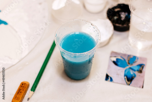 Plastic cup with blue paint for drawing on a white table