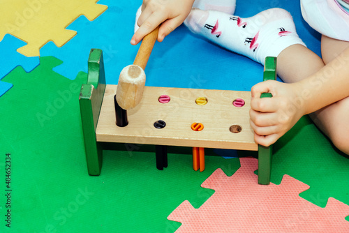 The child plays with a multi-colored children's toy with a wooden mallet