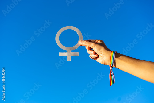 Blue sky background with a hand of a woman with female symbol in favor of feminism, fighting in favor of women, Female strength, LGTB flag