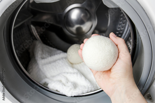 Woman using wool dryer balls for more soft clothes while tumble drying in washing machine concept. Discharge static electricity and shorten drying time, save energy. photo
