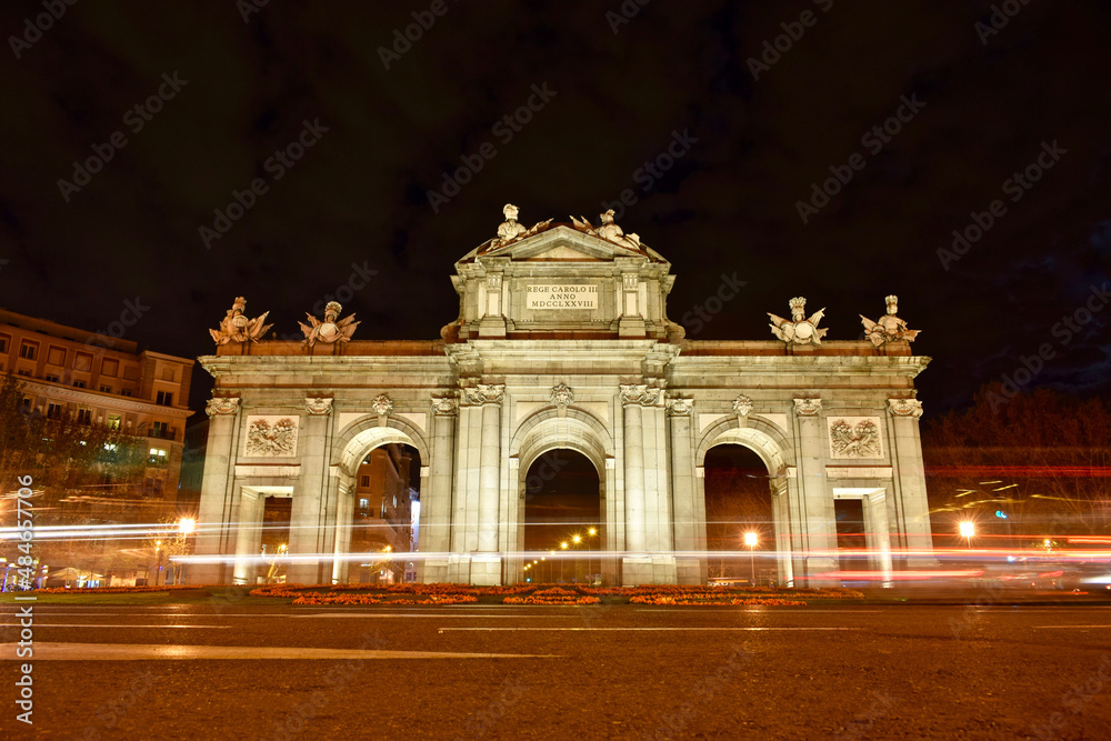 Puerta de Alcala at night and full moon. Light trail effect of vehicles passing through the Puerta de Alcala at night with full moon. Front view from the front.