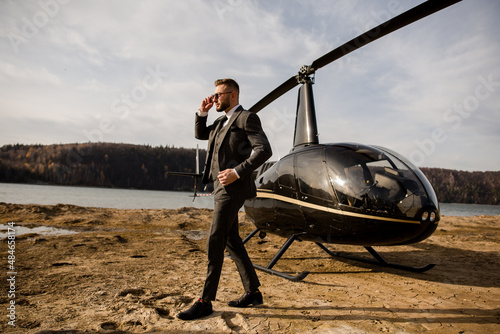 Rich man talking on the phone with business partners. Helicopter stands on the beach photo