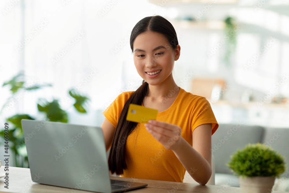 Happy asian lady with laptop and credit card sitting at table, purchasing goods in web store and smiling, free space Happy asian lady with laptop and credit card sitting at table, purchasing goods in web store and smiling, free space