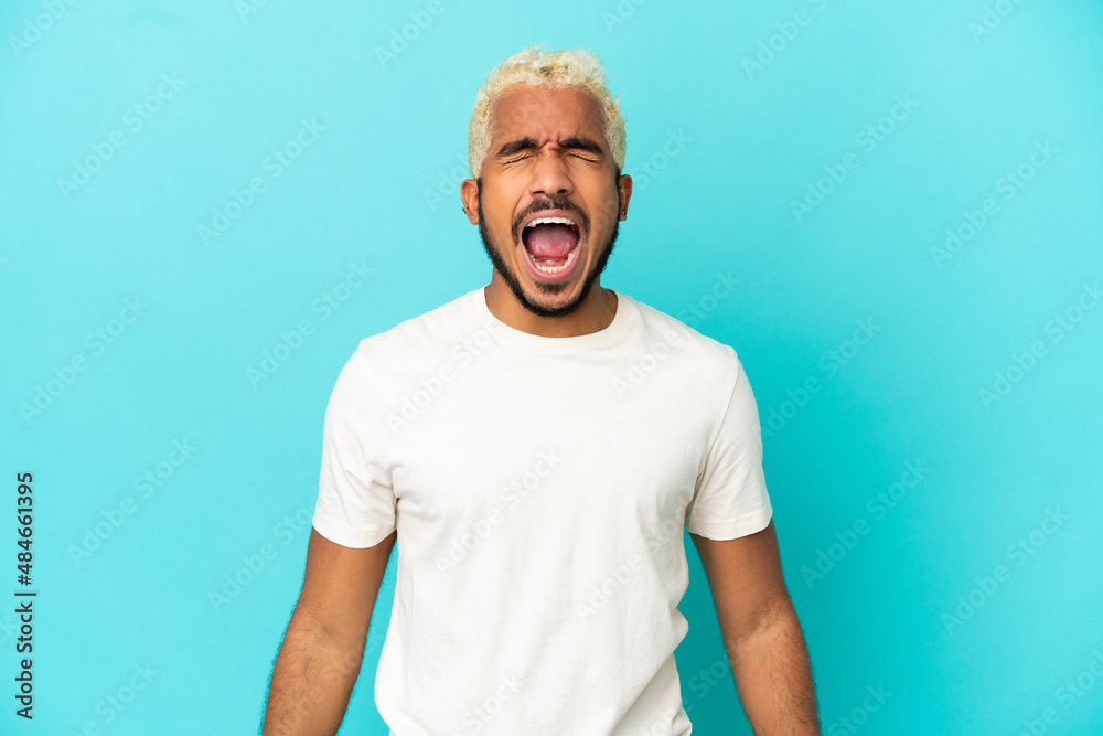 Young Colombian handsome man isolated on blue background shouting to the front with mouth wide open