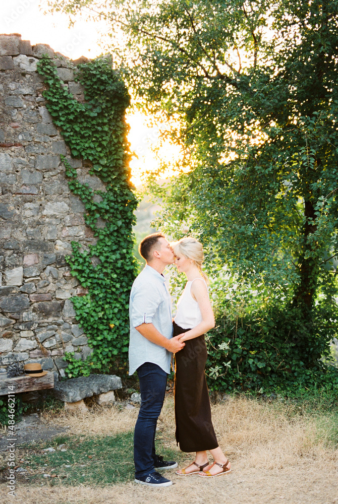 Man kisses woman on the forehead while standing by a stone wall