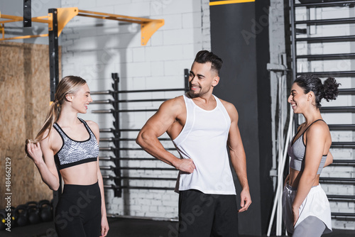 Positive sportsman standing near multiethnic sportswomen in gym.