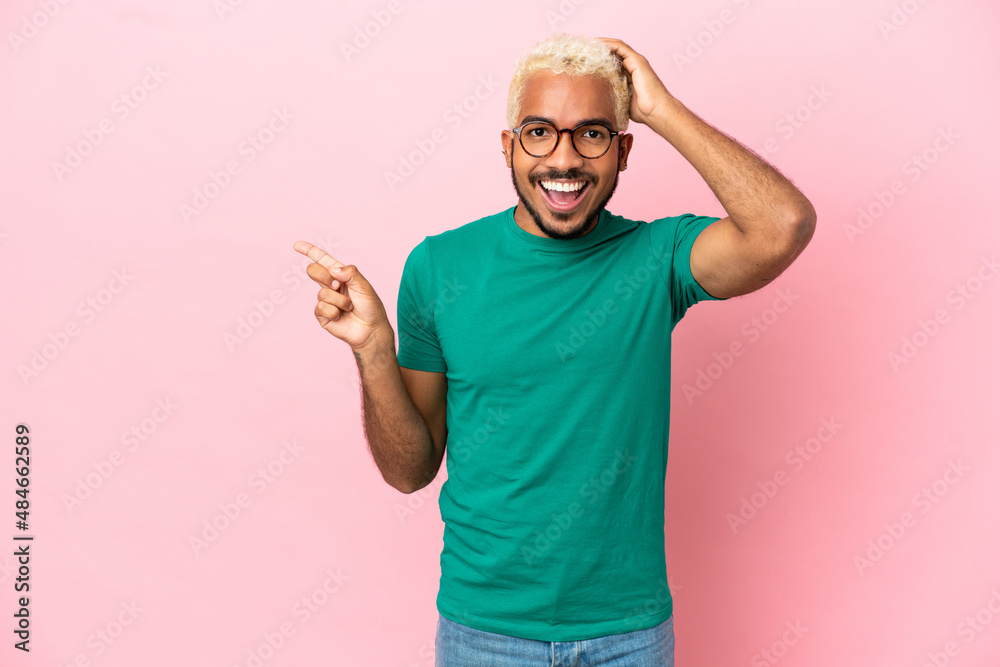 Young Colombian handsome man isolated on pink background surprised and pointing finger to the side Young Colombian handsome man isolated on pink background surprised and pointing finger to the side