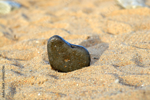 Heart shape stone against background of beach. Summer sunny day. Love, wedding and Valentine day concept. Finding beautiful and interesting stones. Beach vacation. 