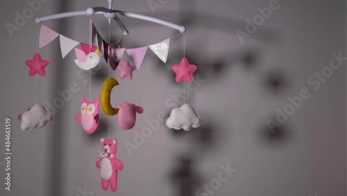 baby mobile with pink hand-stitched animal and bird toys with yellow moon on white wall background. spinning on the baby's crib in the room
