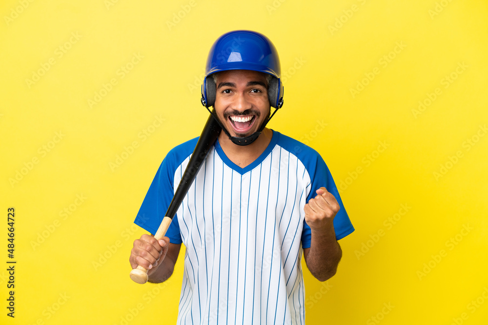 Young Colombian latin man playing baseball isolated on yellow background celebrating a victory in winner position